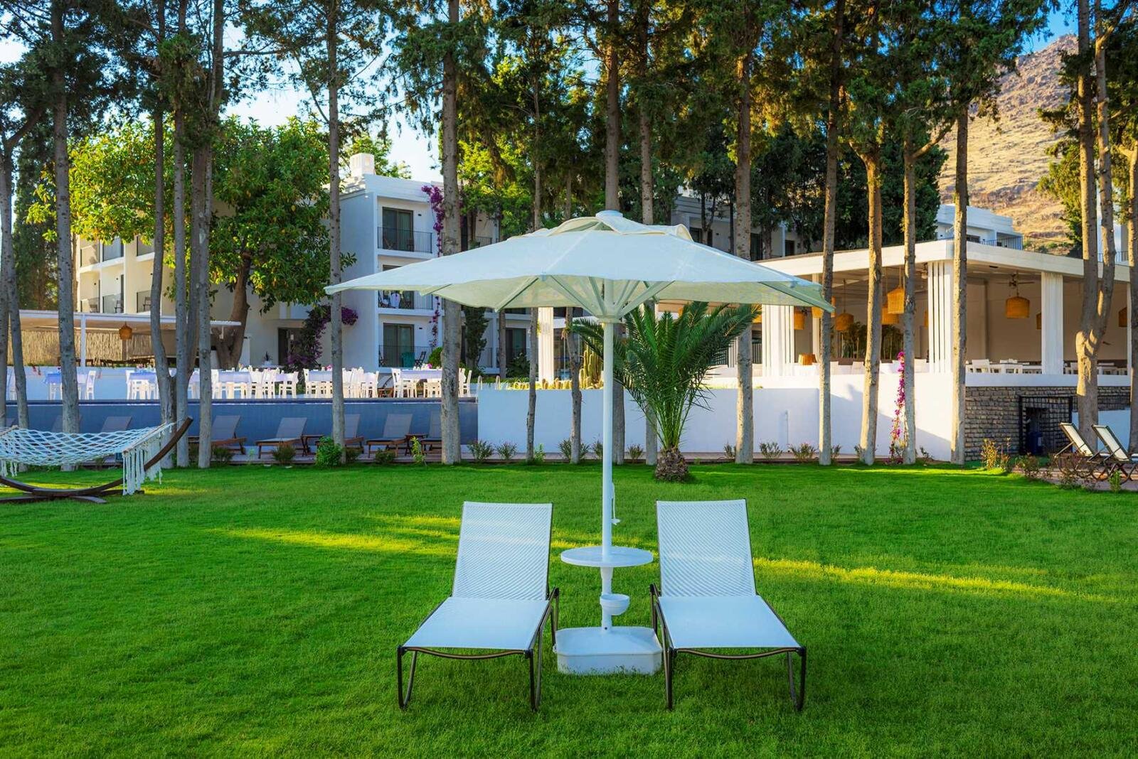 Hotelrenovierung Bodrum mit großzügigem Hotelgarten, Rasenfläche und schattenspendenden Bäumen.