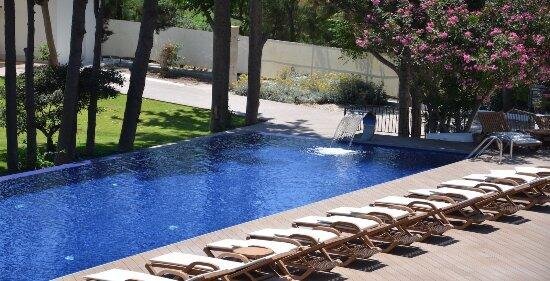 Poolbereich des LIV Hotel by Bellazure mit Sonnenliegen, Bäumen und mediterraner Gartenanlage.